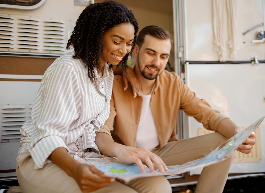 RV Insurance - A Young Couple Looking at a Map While Sitting in Front of an RV While Traveling Across Country at Sunset