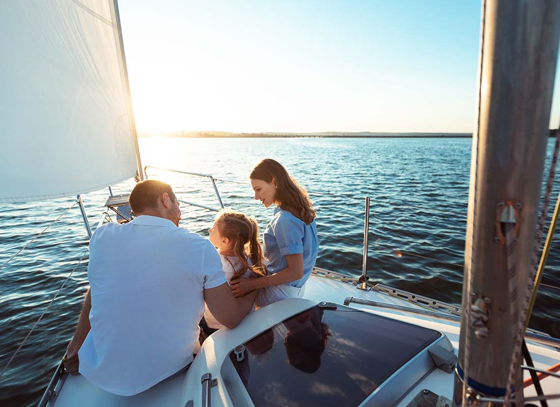 Yacht Insurance - Back View of Young Family of Three Sitting on a Yacht Deck While Sailing at Sunset